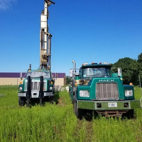 Two green Herr Well Drilling rig trucks parked in an open field for farm well pump installation near Watertown, WI