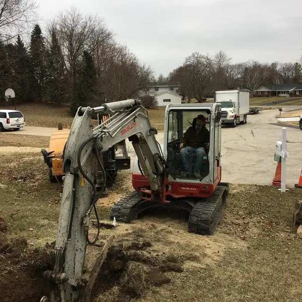 Operator opening a shallow utility trench with a compact excavator in a residential neighborhood