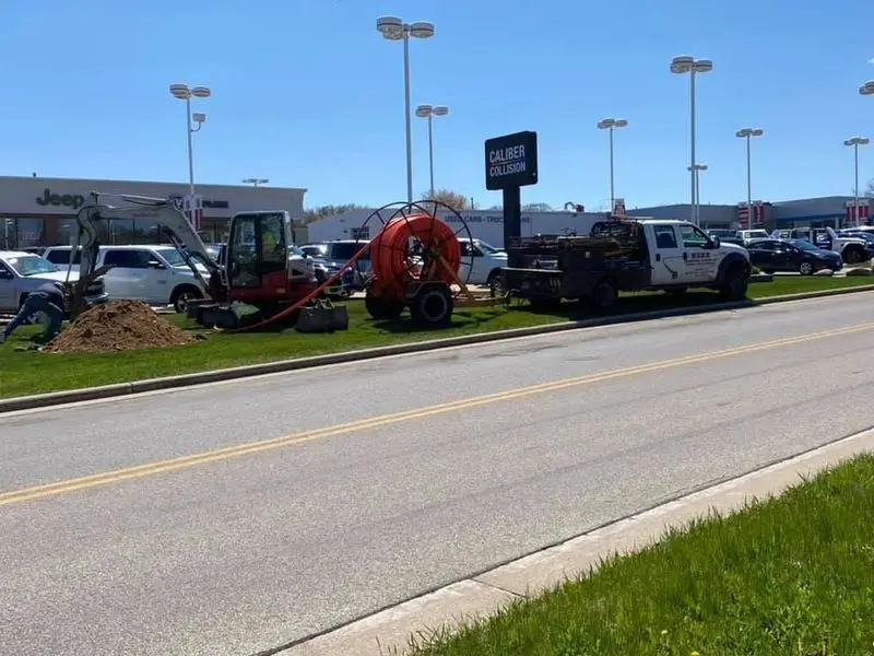 Herr Drilling excavator, conduit reel, and service truck working a commercial site beside a main road