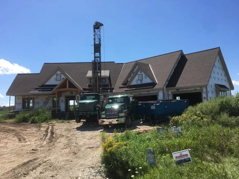 Drilling rig in front of a partially constructed house on a sunny day.
