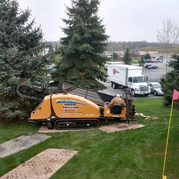 Yellow horizontal directional drilling machine in operation on a grassy area; person in driver's seat.