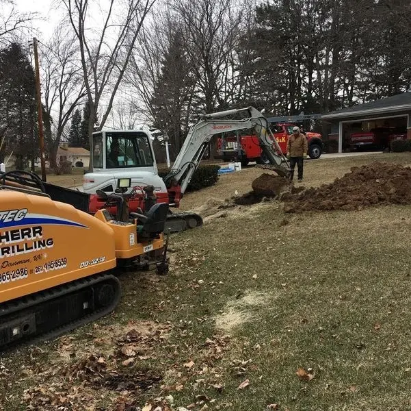 Excavator and drill equipment set up in a residential yard for well drilling work in New Berlin, WI