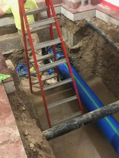 New blue water service pipe and an access ladder in an open trench at a building foundation
