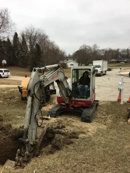 Excavator opening a backyard well pit ahead of a well pump installation on a Brookfield, WI property