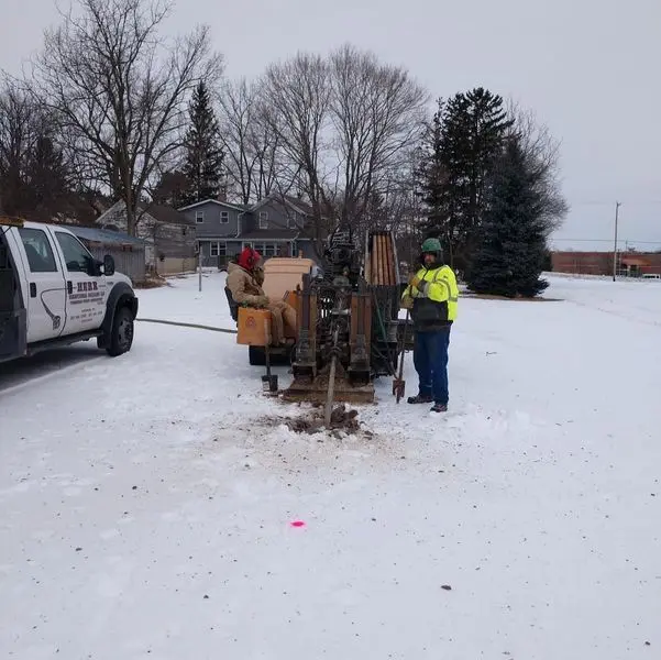 Herr Well Drilling crew running a small drill rig in the snow beside their service truck